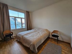 een slaapkamer met een bed en 2 stoelen en een raam bij Lovely city center apartment with amazing views and free parking! in Tromsø