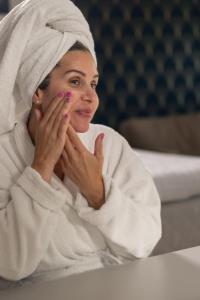 a woman in a towel laying on a bed looking at her face at Säröhus Hotel, Conference & Spa in Särö