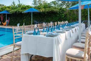 a row of white tables with chairs and a pool at Eleni Family Apartments in Sidari