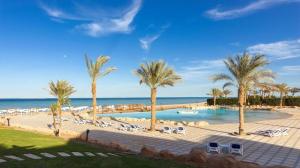 Apartment inside 5* star hotel private beach with reef (FOREIGNERS ONLY) في الغردقة: مسبح فيه نخيل وكراسي والمحيط