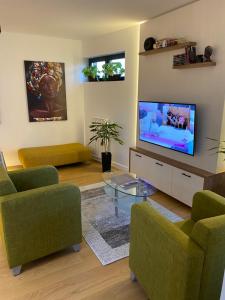 a living room with a flat screen tv and green chairs at Vrtovi Ceraka in Belgrade