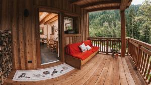 porche de una cabaña de madera con sofá rojo en B&B Maso Ghirola, en Pinzolo