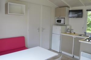 una pequeña cocina con armarios blancos y un sofá rojo en camping Le moulin, en Patornay