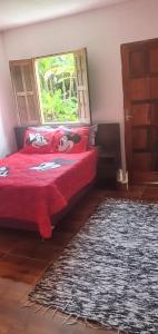 a bedroom with a red bed with a window and a rug at SITIO RECANTO DOS PASSAROS in Itacaré