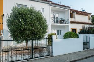 a white house with a fence and a tree at Raminhos Guest House in Vila Nova de Milfontes