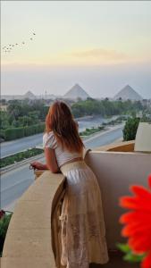 Uma mulher de vestido, sentada num parapeito, a olhar para um rio. em Pyramids sunrise inn no Cairo