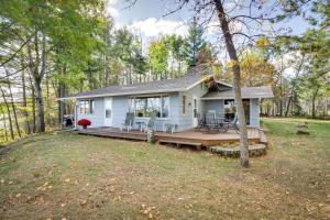 une maison blanche avec une terrasse dans les bois dans l'établissement Lakefront Park Rapids Cabin with Grill and Fire Pit!, à Park Rapids