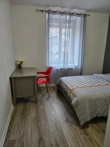 1 dormitorio con cama, escritorio y silla roja en PROCHE DU CENTRE VILLE, "Le Voltaire " TOUTES COMMODITES, OYONNAX, en Oyonnax