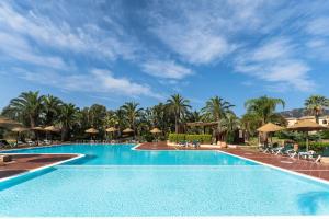 a pool at a resort with palm trees and umbrellas at Apartments in residence with swimming pool in Santa Margherita di Pula, 250 meters from the sea in Pula