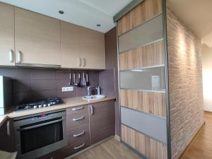 La cuisine est équipée de placards en bois et d'un four avec plaques de cuisson. dans l'établissement 3M Bridge apartment SELF CHECK-IN, à Kaunas