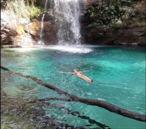 a person swimming in a pool in front of a waterfall at Villa de Assis Suítes in Alto Paraíso de Goiás