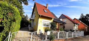 a yellow house with a red roof behind a fence at Adikati Lak in Bük