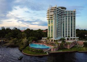 a large building with a swimming pool next to a river at Hotel Tropical Executive Flat 020 in Manaus
