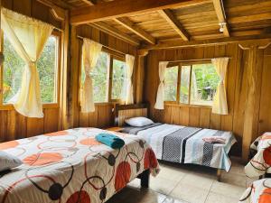 2 camas en una habitación con paredes y ventanas de madera en La Casa de Cecilia Mindo, en Mindo