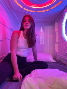une femme assise sur un lit dans une pièce avec des lumières roses dans l'établissement Galactic Star Wars Sleep Pods For Eight With Pool, à Pacific