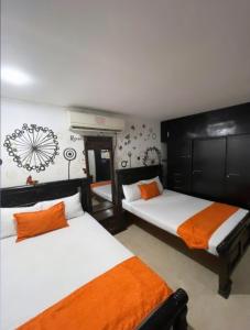 una camera con 2 letti con lenzuola bianche e arancioni di Casa Turística Realismo Mágico a Aracataca