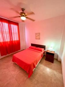 a bedroom with a red bed and a ceiling fan at Casa con piscina y salida a la playa in Playas