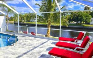 eine Terrasse mit roten und weißen Stühlen und einem Pool in der Unterkunft House Rainbow in Cape Coral