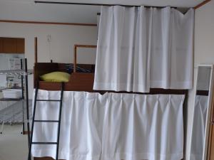um beliche com uma cortina branca num quarto em コウノトリの里の宿 em Fukiage