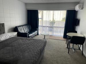 a bedroom with a bed and a couch and a table at Aaron Court Motel Whangarei in Whangarei