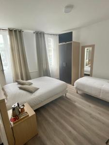 1 dormitorio con 2 camas, mesa y ventanas en Hôtel Du Commerce en Fécamp