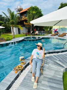 a man sitting in a chair next to a swimming pool at Bum King Resort Hồ Tràm in Xuyên Mộc