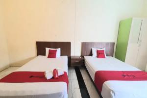 two beds in a hotel room with red pillows at RedDoorz near Universitas PGRI Kanjuruhan in Gadang