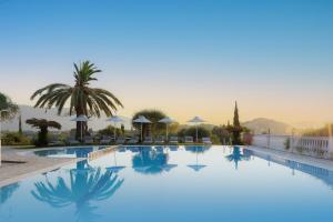 a pool at a resort with palm trees and mountains in the background at Paradise Hotel Corfu in Gouvia