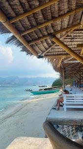 a person sitting on a bench on a beach at Bronze Bungalows in Gili Meno