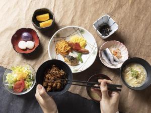 een persoon met eetstokjes over een tafel met borden voedsel bij Mitsui Garden Hotel Okayama in Okayama
