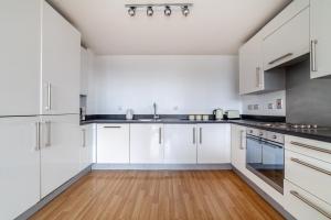 a kitchen with white cabinets and a wooden floor at The Stratford Collection in London