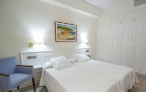 a white bedroom with a bed and a blue chair at Hotel Llafranch in Llafranc