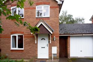 ein Backsteinhaus mit einer weißen Tür und zwei Fenstern in der Unterkunft 3 Bedroom Home in Central Milton Keynes in Loughton