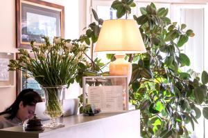 une femme assise sur un bureau avec un vase de fleurs dans l'établissement Hotel Franceschi, à Forte dei Marmi