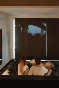duas pessoas sentadas numa cama a olhar para uma televisão em VIBE LUXURY CABINS em Arnuero