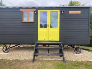 a tiny house with a yellow door and a ladder at The Hive Shepherds hut in Offton