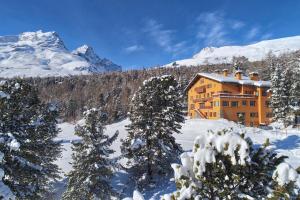 an orange building in the snow with trees and mountains at Hotel Chesa Spuondas in St. Moritz