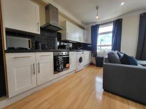 una cocina con armarios blancos y un sofá en una habitación en Tooting Bec Central Apartment by London Tube, en Londres