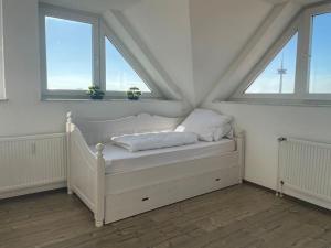 białe łóżko w pokoju z 2 oknami w obiekcie Über den Dächern von Essen w Essen