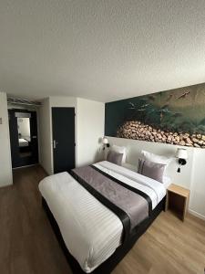 a bedroom with a large bed with a painting on the wall at Logis Cris Hôtel, Lyon Est in Corbas