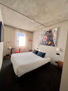 a bedroom with a large white bed with a painting on the wall at Théo Hôtel Limoges, The Originals City in Limoges