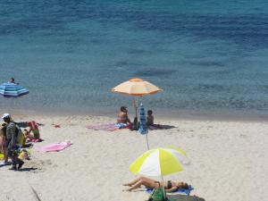 a group of people sitting on the beach under umbrellas at Le Colline di Isola Rossa in Trinità d'Agultu e Vignola