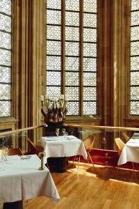een eetkamer met 2 tafels en glas-in-loodramen bij Kruisherenhotel Maastricht - Oostwegel Collection, member of Design Hotels in Maastricht