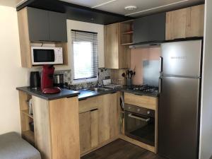 La cuisine est équipée d'armoires en bois et d'un réfrigérateur en acier inoxydable. dans l'établissement camping les sables du midi, à Valras-Plage