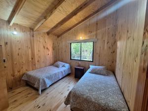 two beds in a room with wooden walls at Cabañas piedra Alta, Huilo Huilo in Panguipulli