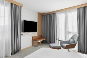 a hotel room with a bed and a tv and a chair at Courtyard by Marriott Biel Bienne in Biel