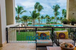 balcón con vistas a la piscina y a las palmeras en Hermoso y perfecto 2 Hab frente al mar en Cap Cana en Punta Cana