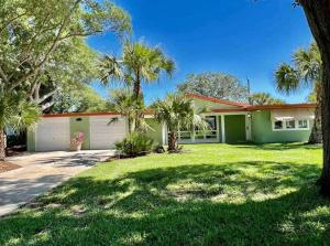 a green house with palm trees in a yard at Sea la Vie - Beach Town Charm+Newly Renovated in Cocoa Beach