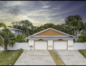 uma casa branca com duas portas de garagem e uma cerca em Adam's Retreat - 5 min from Beach - 2bed/2bath em Cape Canaveral