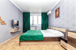 een slaapkamer met een bed met groene lakens en een televisie bij Квартира в престижном районе в новостройке in Pavlodar